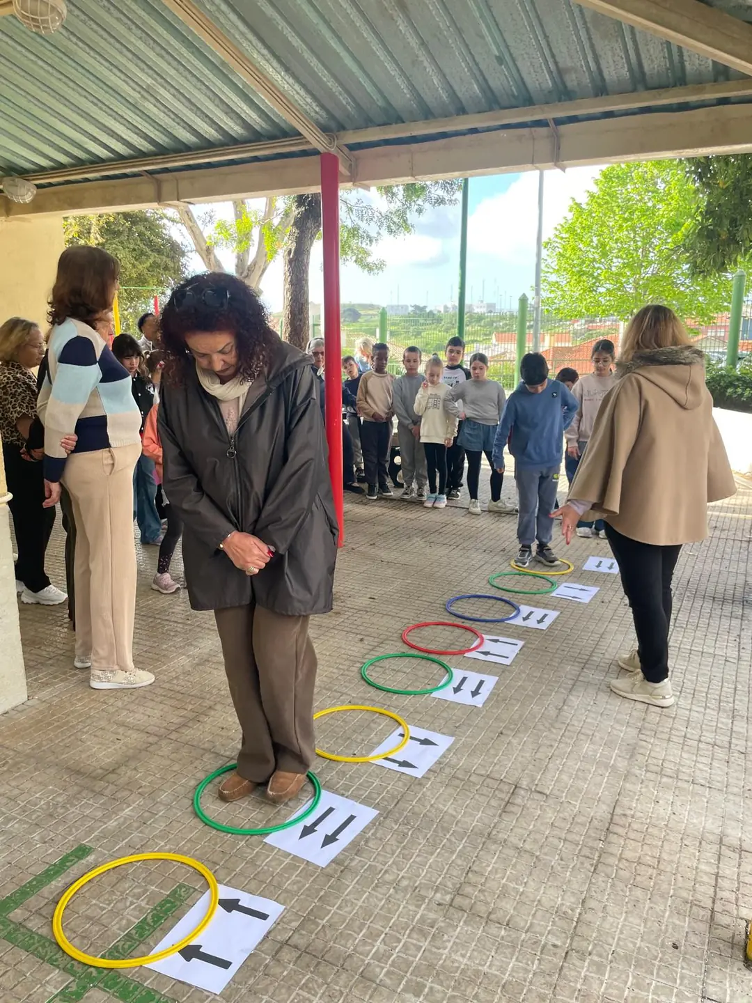 Une participante de l’Académie Senior joue au jeu des cerceaux colorés posés au sol, pendant que des enfants et d’autres seniors attendent leur tour.